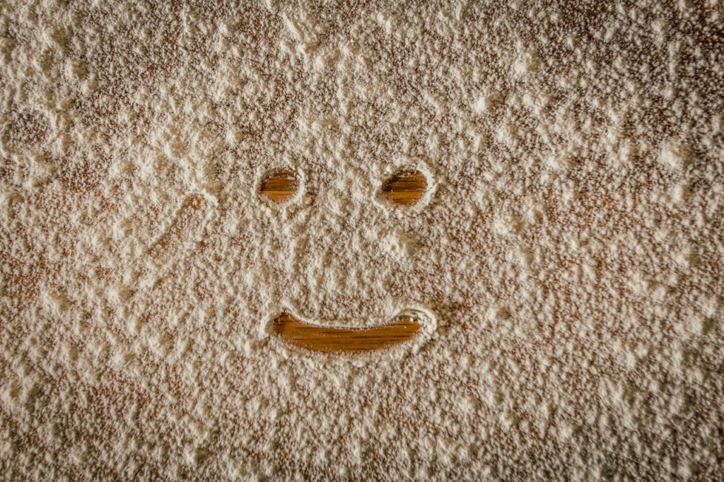 Ein von weißem Mehl bedeckter Holz- Untergrund in dem ein lächelndes Gesicht gemalt wurde. 