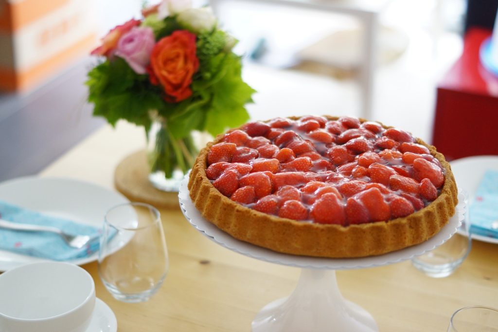 Ein klassischer Sommerkuchen: Erdbeeren auf einem Bisquitboden, serviert auf einer kleinen Kuchenplattform mit Fuß.