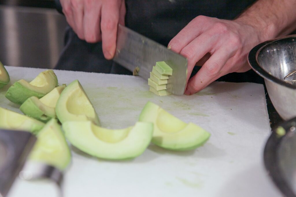 Eine Avocado wird mit einem großen Kochmesser in kleine Stücke geschnitten.