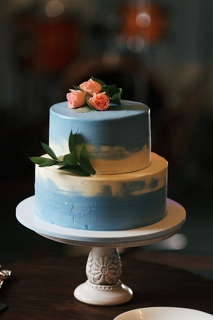Auf einer Kuchenplatte steht ein zweistöckiger Hochzeitskuchen, der hellblau eingefärbt wurde.